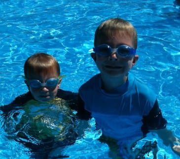 Two young boys in a pool with goggles on.