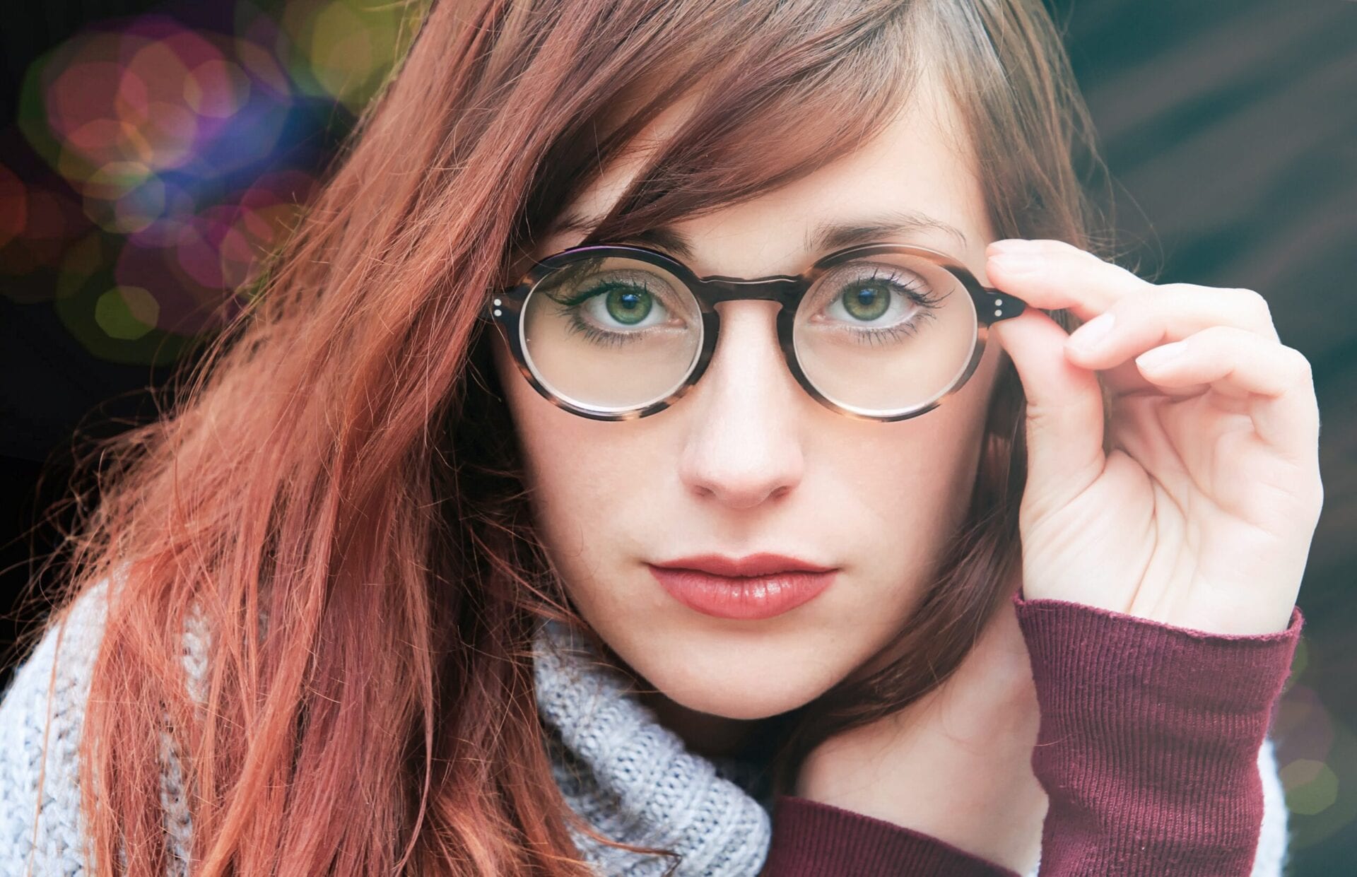 A woman with glasses and red hair wearing a sweater.